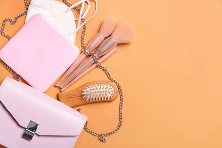 Medical mask with case, makeup brushes and bag on color background