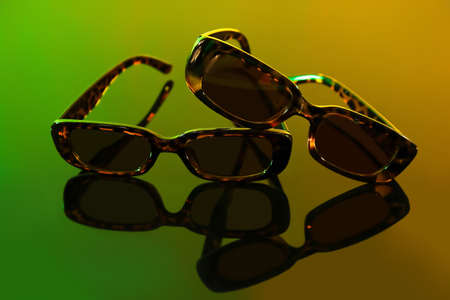Stylish female sunglasses on color background