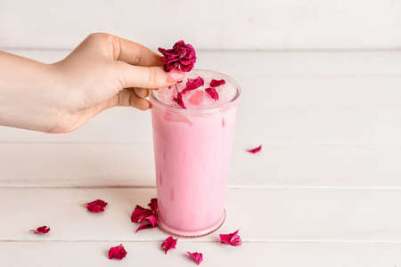 Woman decorating tasty rose latte with flower petals on tableの写真素材