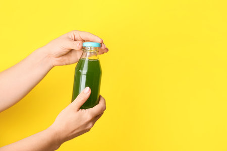 Female hands with bottle of healthy juice on color backgroundの写真素材