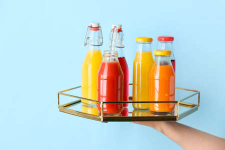 Female hand with bottles of healthy juice on color background