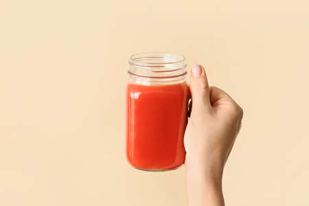 Female hand with mason jar of healthy juice on color background