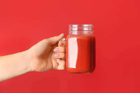 Female hand with mason jar of healthy juice on color background