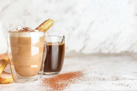 Glass of tasty Tiramisu Latte and jug with coffee on light backgroundの写真素材