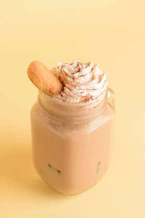 Mason jar of tasty Tiramisu Latte on beige background