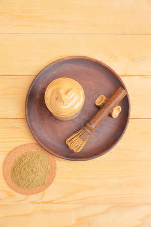 Glass of tasty dalgona hojicha latte, powder and chasen on wooden backgroundの写真素材
