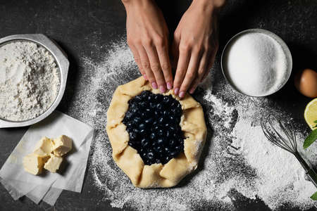 Woman cooking blueberry galette on dark background