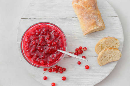 Bowl with red currant jam and bread on light background