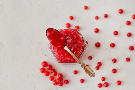 Jar of red currant jam and berries on light background