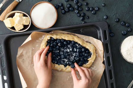 Woman with uncooked blueberry galette on dark background