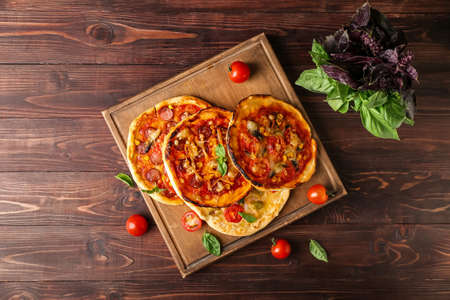 Board with delicious mini pizzas on wooden background