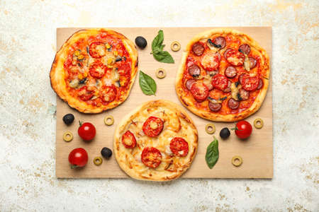 Board with delicious mini pizzas on light background