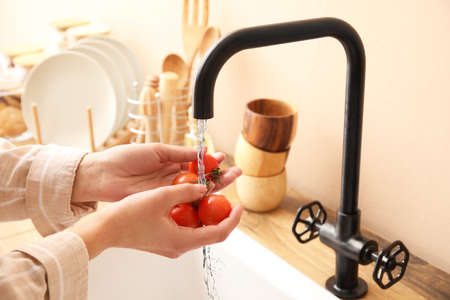 Woman washing fresh tomatoes in kitchen sink, closeup
