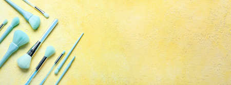 Set of blue makeup brushes on yellow background with space for text