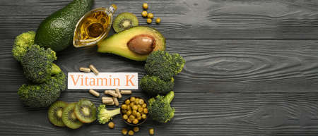 Text VITAMIN K with healthy products and pills on wooden background with space for text