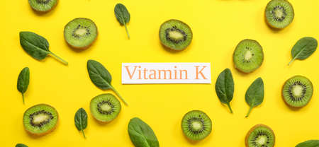 Text VITAMIN K with green spinach leaves and kiwi slices on yellow background
