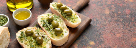 Slices of bread with tasty olives, oil and herbs on color background with space for textの写真素材