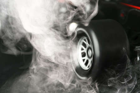 Modern racing car with smoke from under wheels on dark background, closeupの写真素材