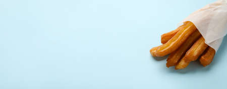 Tasty churros in parchment on blue background with space for text