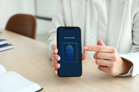 Woman holding smartphone with locked screen while sitting at workplace, closeup