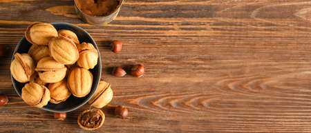 Bowl of tasty walnut shaped cookies with boiled condensed milk on wooden background with space for...