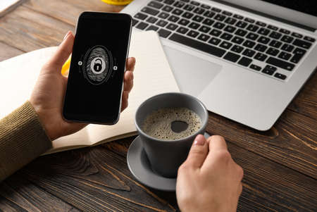 Woman with coffee and smartphone using fingerprint scanner to login into personal account at...