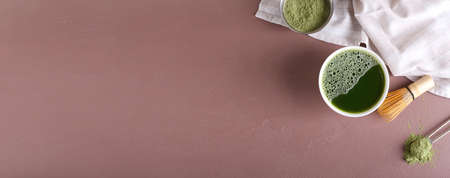 Cup of matcha tea, chasen and powder on brown background with space for text