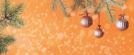 Beautiful Christmas balls hanging on coniferous branch against orange background