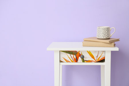 Stylish small table with books and cup near color wall in room
