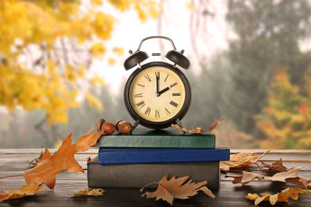 Alarm clock, books and autumn leaves on table outdoorsの写真素材