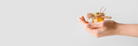 Female hand holding jar of sweet honey on light background with space for textの写真素材