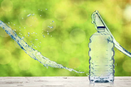 Bottle of fresh water with splashes on wooden table outdoorsの写真素材