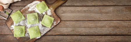 Board with raw green ravioli on wooden background with space for textの写真素材