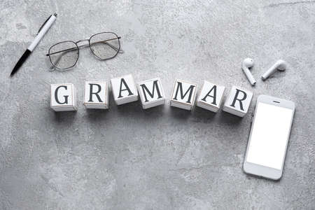 Word GRAMMAR made of cubes, phone, pen, earphones and glasses on gray backgroundの写真素材