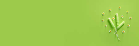 Menstrual tampons and chamomile flowers on green background with space for text