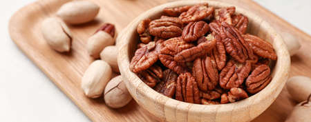 Bowl with tasty pecan nuts on light background, closeup