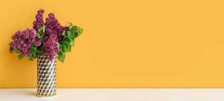 Vase with bouquet of beautiful lilac on table against orange background with space for text