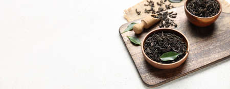 Bowls with dry black tea leaves on light background with space for text