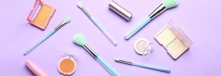 Different makeup brushes and cosmetic products on lilac background. Banner design