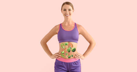 Sporty young woman with healthy products on her body against pink background. concept of dietの写真素材
