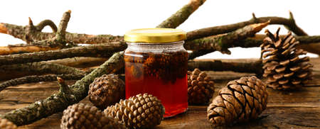 Jar of tasty pine cone jam and tree branches on wooden table