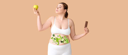 Oversize woman with fresh apple, sweet chocolate and healthy products on her body against color background. concept of dietの写真素材