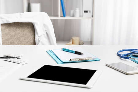Clipboard, tablet computer, mobile phone and pills on table in doctor's office