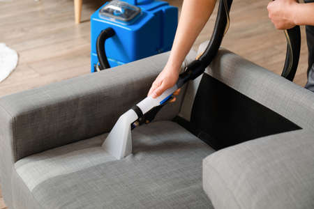 Man removing dirt from gray sofa with vacuum cleaner in roomの写真素材