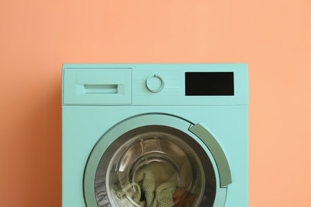 Modern turquoise washing machine near beige wallの写真素材