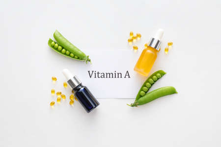 Bottles of essential oil, capsules, green peas and paper sheet with text VITAMIN A on white...