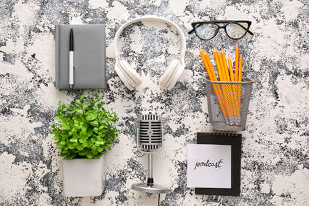 Microphone, headphones, paper with word PODCAST and eyeglasses on grunge background