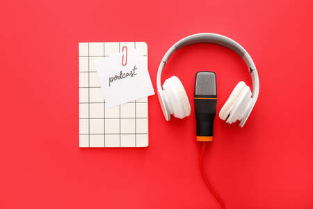 Headphones, microphone, notebook and paper sheet with word PODCAST on color backgroundの写真素材