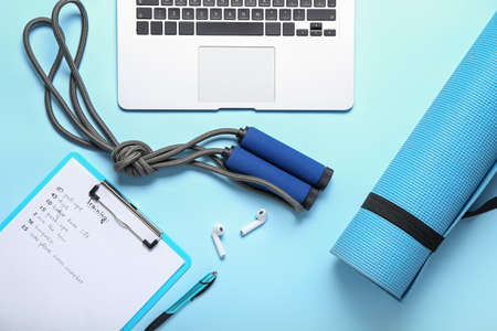 Clipboard with training plan, skipping rope, mat and laptop on blue background