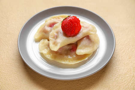 Plate with strawberry dumplings on color background, closeup